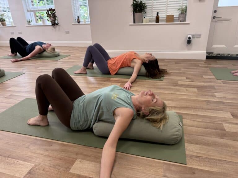 three women laying on bolster cushions in the Shine at the Hollies yoga studio practising Yin Yoga