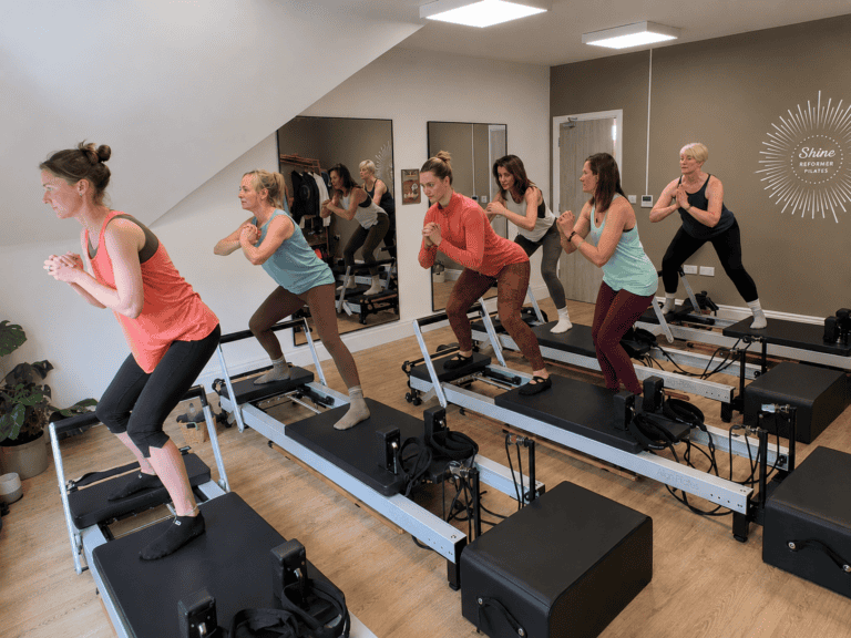 Group of women doing a standing flow movement exercises on reformer pilates machines in a Reformaer Pilates Class at Shine at The Hollies
