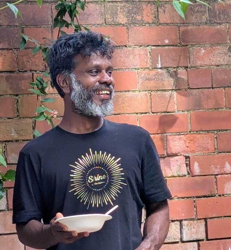 smiling man standing outside in front of a brick wall, called Upali, yoga & Pilates teacher at Shine at The Hollies