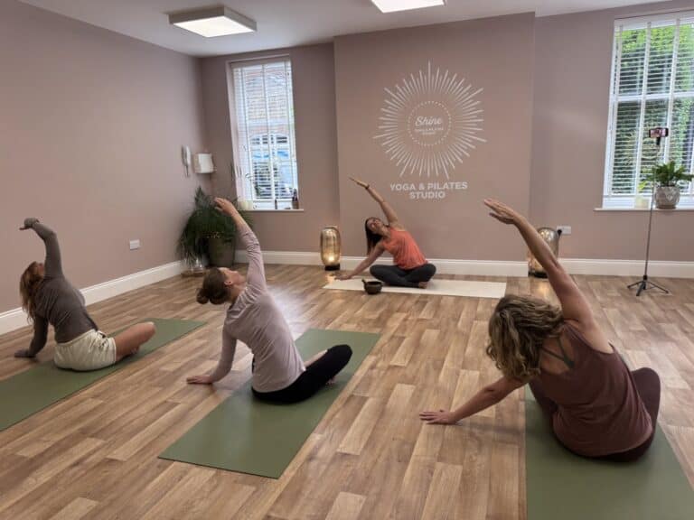 group of people siting in a half lotus position following the yoga teacher in a kundalini class at Shine at The Hollies