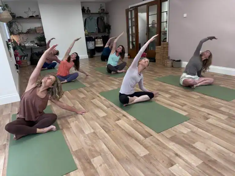 Group of men and women sitting on yoga mats in the Shine at The Hollies yoga studio practising a yoga class