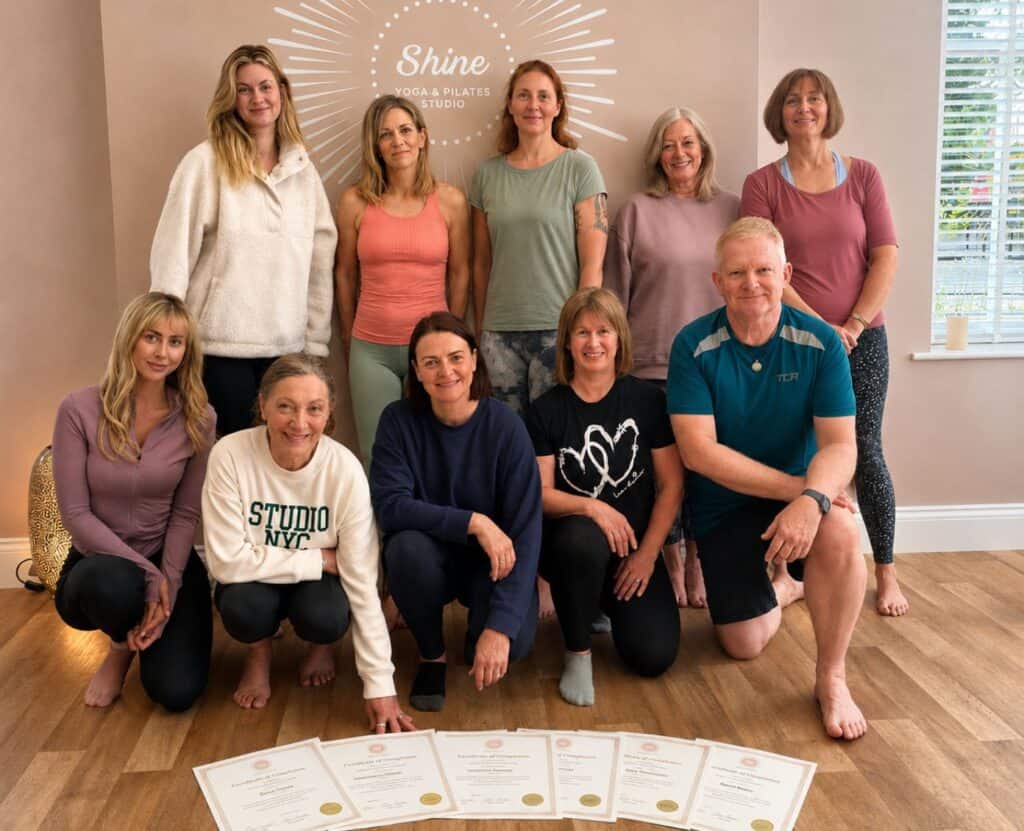 Groups of men and women standing and kneeling together infront of a row of certificates on the floor to show they have graduated from the Mat Pilates Teacher Training course at Shine at The Hollies