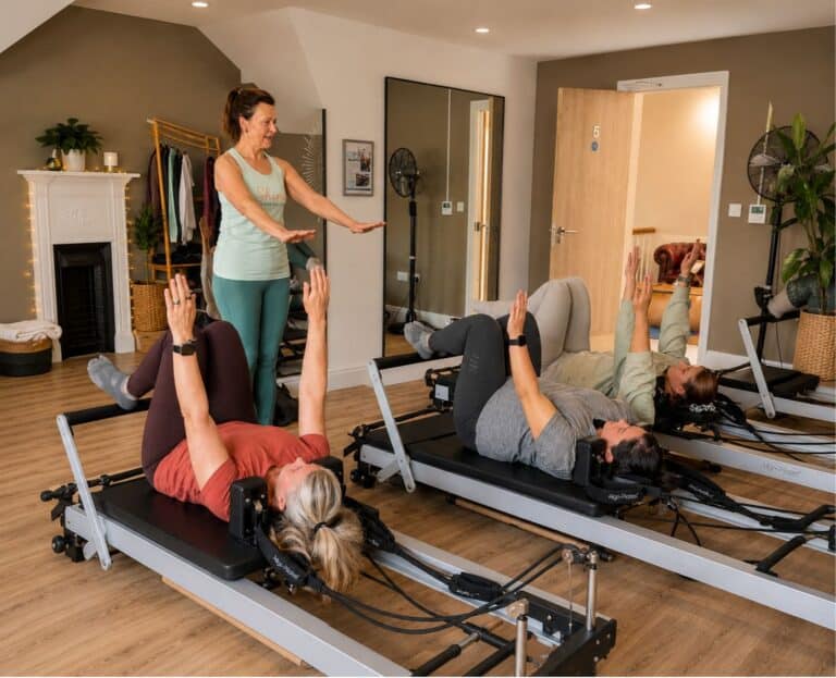 Tabitha Wright owner of Shine at The Hollies demonstrating an exercise to three women laying on Reformer Pilates machines in the Reformer Pilates Teacher Training course